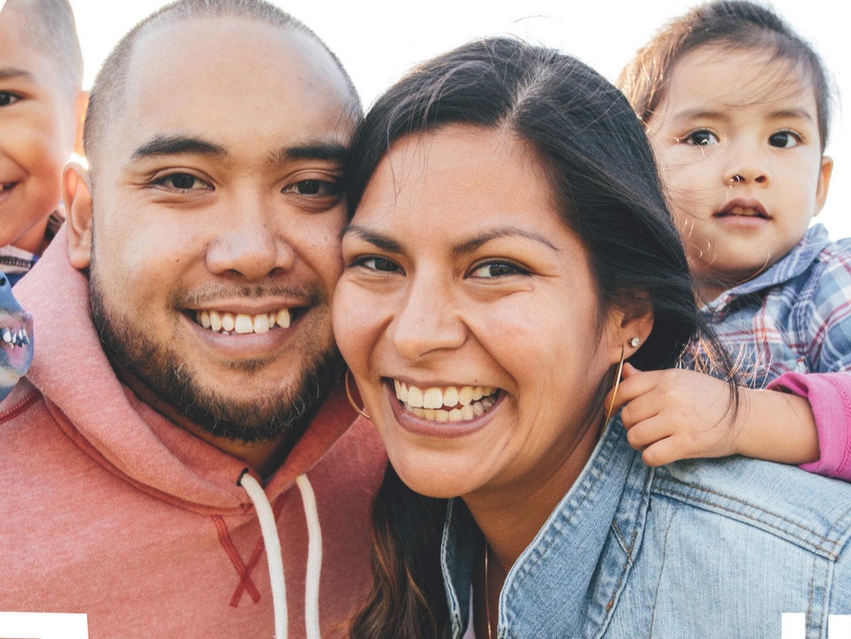 Eine Familie mit zwei kleinen Kindern lächelt in die Kamera